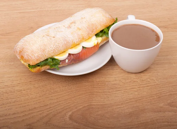 Coffee cup and Real sandwich with smoked salmon, eggs and green on a wooden background. — Stock Photo, Image