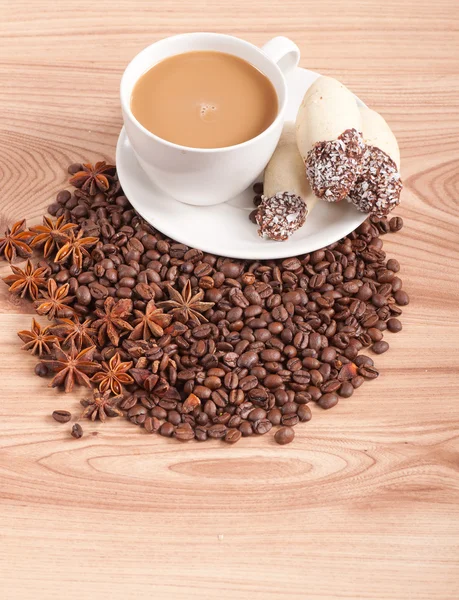 Coffee cup, anise on coffee beans, sweets on the wooden background — Stock Photo, Image