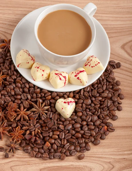 Cup of coffee with beans and white chocolate heart candy over wooden background — Stock Photo, Image