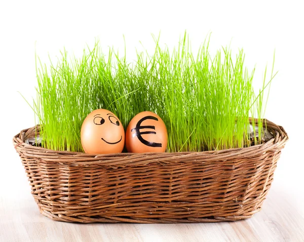 Funny smiling egg with golden euro egg in basket with grass. — Stock Photo, Image