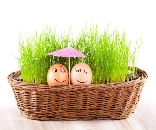 Dos Divertidos huevos sonrientes bajo paraguas en cesta con hierba. baño de sol . — Foto de Stock