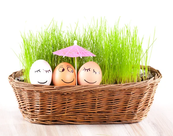 Tres Divertidos huevos sonrientes bajo paraguas en cesta con hierba. baño de sol . — Foto de Stock