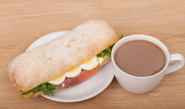 Coffee cup and Real sandwich with smoked salmon, eggs and green on a wooden background. — Stock Photo, Image