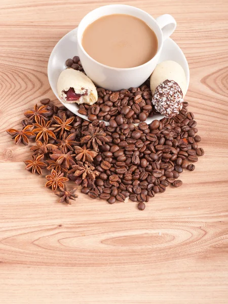 Coffee cup, anise on coffee beans, sweets on the wooden background — Stock Photo, Image