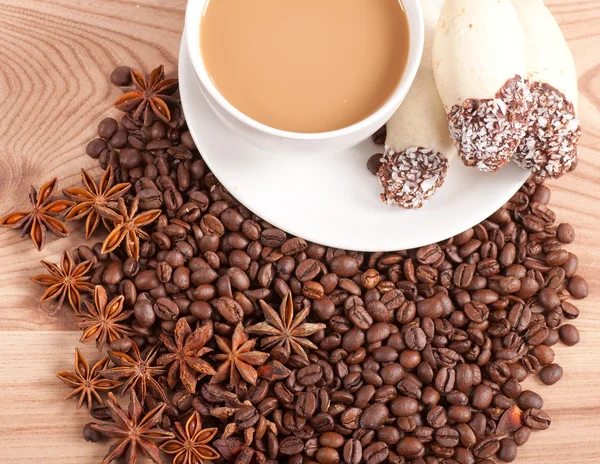 Coffee cup, anise on coffee beans, sweets on the wooden background — Stock Photo, Image