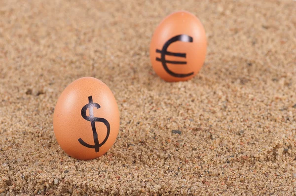 Obrázek velkých bílých vajec s dollarand euro podepisuje na písku. — Stock fotografie