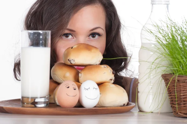 Mooie vrouw met melk, broodje en Pasen mandje van gras — Stockfoto