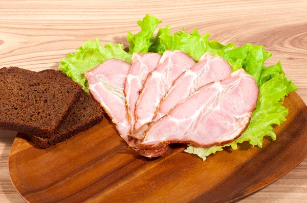 Prosciutto e lattuga con pezzo di pane su un piatto di legno — Foto Stock