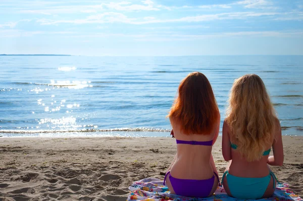 Twee mooie jonge vrouwen zittend op een handdoek op een strand — Stockfoto