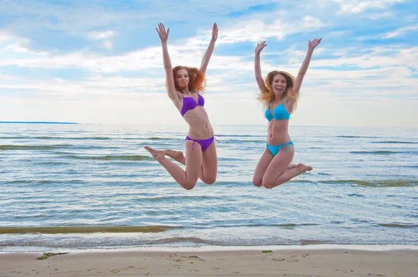 Happy excited young women in bikini jumping on beach — Stock Photo, Image