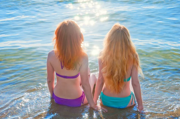 Zwei schöne junge Frauen sitzen im Wasser an einem Strand. — Stockfoto