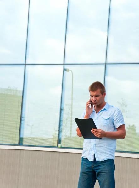 Uomo d'affari con notebook e telefono cellulare di fronte al moderno edificio aziendale — Foto Stock