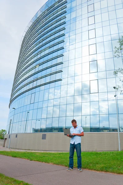 Homem de negócios com laptop na frente do edifício de negócios moderno — Fotografia de Stock