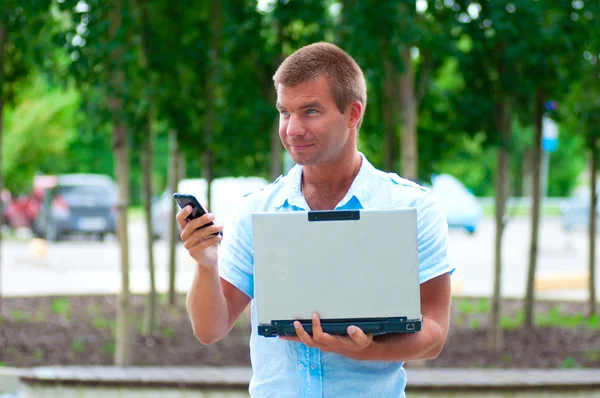 Бізнесмен з ноутбуком і мобільним телефоном перед сучасною бізнес-будівлею — стокове фото