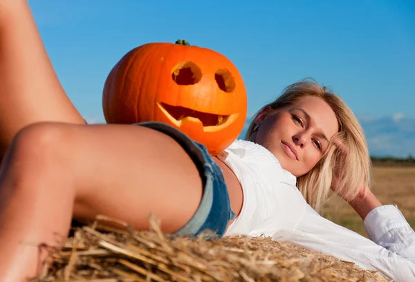 Beautiful woman posing on a bale with pumpkin — Stock Photo, Image