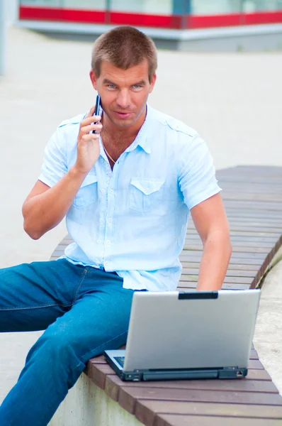 Homem de negócios com laptopand telefone móvel na frente do edifício de negócios moderno — Fotografia de Stock