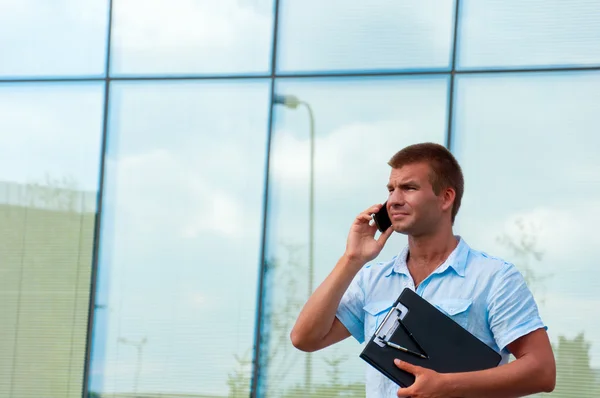 Iş adamı ile defter ve modern işletme binası önünde hareket eden telefon — Stok fotoğraf