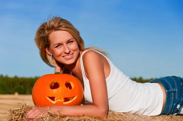 Woman in jeans shorts posing on a bale with pumpkin — Stock Photo, Image