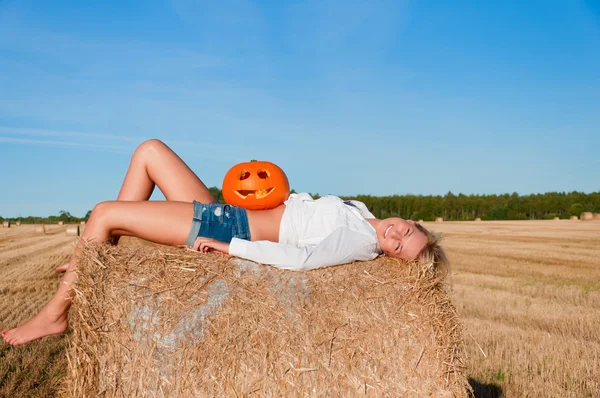 Woman in jeans shorts posing on a bale with pumpkin — Stock Photo, Image