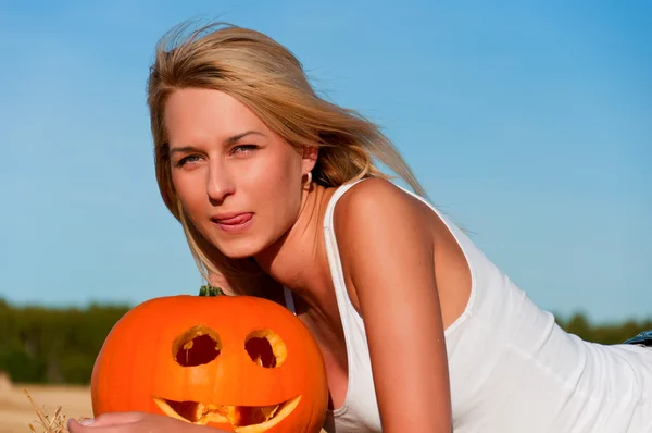 Woman in jeans shorts posing on a bale with pumpkin — Stock Photo, Image