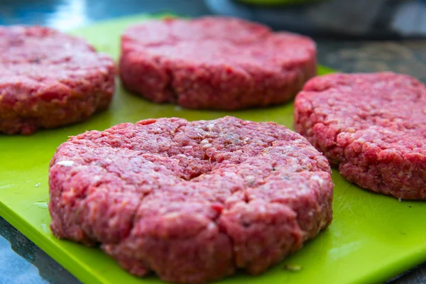 Hambúrgueres de carne crua fechar em uma tábua de corte — Fotografia de Stock