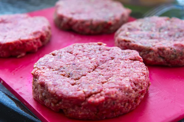 Rå nötkött hamburgare på nära håll på en skärbräda — Stockfoto