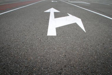 Siyah asfalt üzerinde yön oku olan beyaz yol işaretleri