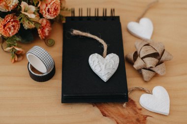 Siyah çarşaflı, kopya alanı olan bir defter, bir buket çiçekli ahşap bir masa ve beyaz bir kalp..