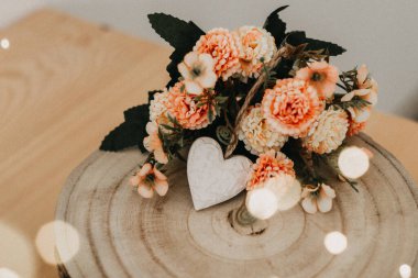 Etrafında bir buket çiçek ve beyaz bir kalp olan ahşap masa..