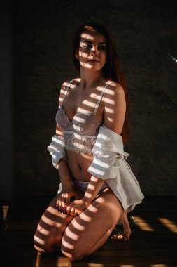 Siyah banyo cüppeli, ince, kızıl saçlı genç bir kız güneşliğin altında güneşlenir.