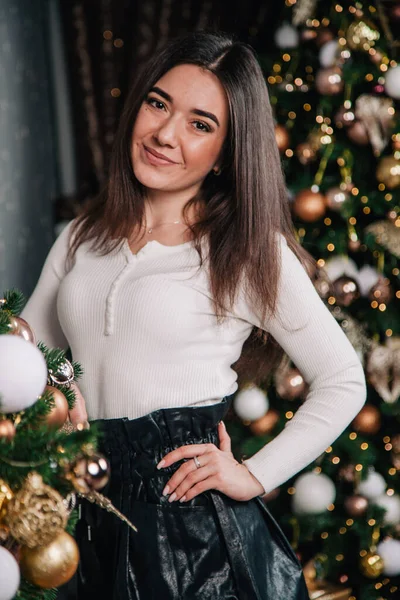Una joven con una blusa blanca y una falda negra junto a la chimenea sobre el fondo de un árbol de Navidad — Foto de Stock
