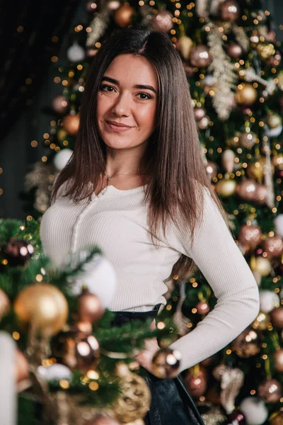Uma jovem de blusa branca e saia preta fica perto da lareira no fundo de uma árvore de Natal — Fotografia de Stock