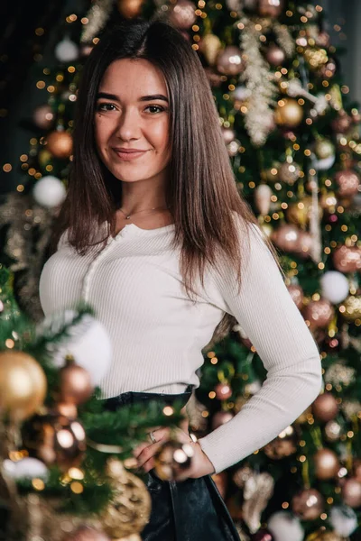 Uma jovem de blusa branca e saia preta fica perto da lareira no fundo de uma árvore de Natal — Fotografia de Stock