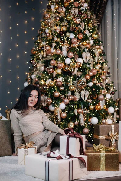 Portrait of a young, beautiful girl in a dress near the Christmas tree with a bunch of gifts — Stock Photo, Image