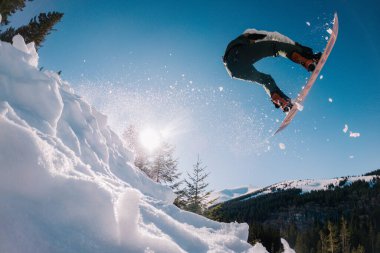 Adamın biri güneşin arka planında bir snowboard 'a atlıyor ve ön taraftan yakalıyor.