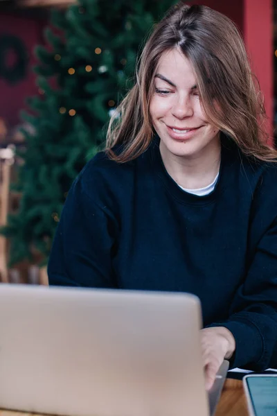 Młoda piękna dziewczyna w czarnym swetrze w kawiarni pracuje z laptopem i telefonem — Zdjęcie stockowe