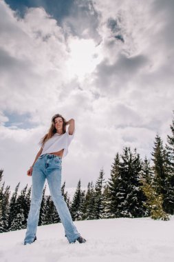 Dağ ormanlarına karşı poz veren modaya uygun giyinmiş güzel beyaz kadın.