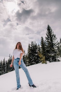 Dağ ormanlarına karşı poz veren modaya uygun giyinmiş güzel beyaz kadın.