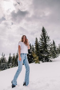 Dağ ormanlarına karşı poz veren modaya uygun giyinmiş güzel beyaz kadın.