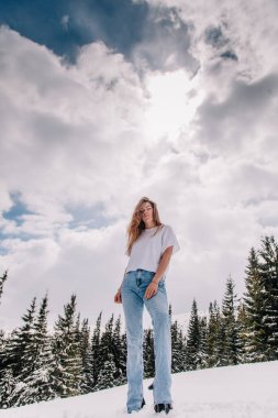 Dağ ormanlarına karşı poz veren modaya uygun giyinmiş güzel beyaz kadın.