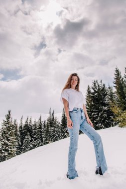 Dağ ormanlarına karşı poz veren modaya uygun giyinmiş güzel beyaz kadın.