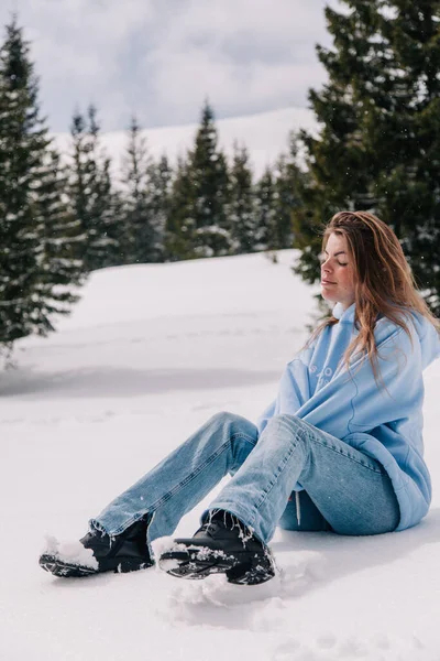 Młoda, piękna dziewczyna w górach siedzi w śniegu pośród drzew — Zdjęcie stockowe