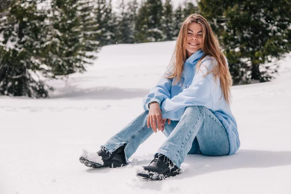 Dağlarda genç, güzel bir kız ağaçların arasında karda oturuyor.