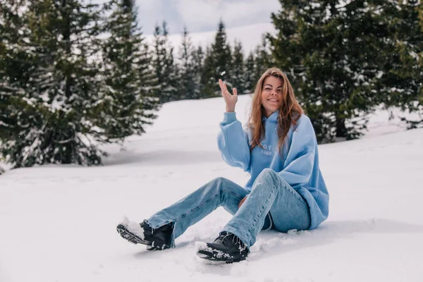 Dağlarda genç, güzel bir kız ağaçların arasında karda oturuyor.