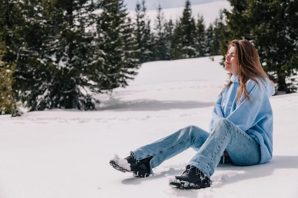 Dağlarda genç, güzel bir kız ağaçların arasında karda oturuyor.