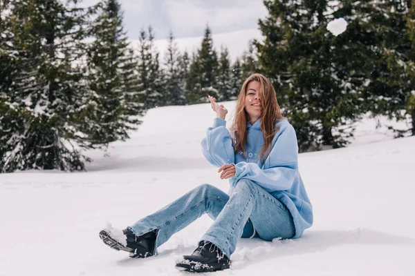 Dağlarda genç, güzel bir kız ağaçların arasında karda oturuyor.