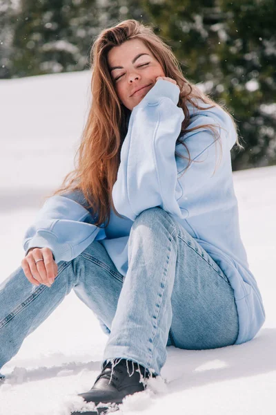 Dağlarda genç, güzel bir kız ağaçların arasında karda oturuyor.