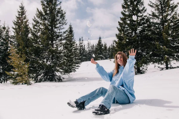 Dağlarda genç, güzel bir kız ağaçların arasında karda oturuyor.