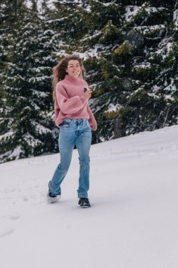 Genç, ince, uzun saçlı bir kız dağlardaki bir kış ormanında karda koşuyor..