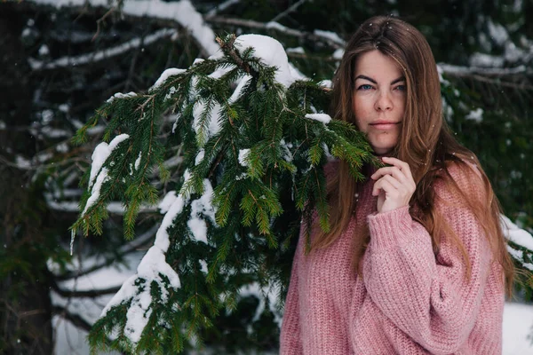 A young, cheerful girl sprinkled with snow under the branches of a spruce tree in the mountains — Stock Photo, Image